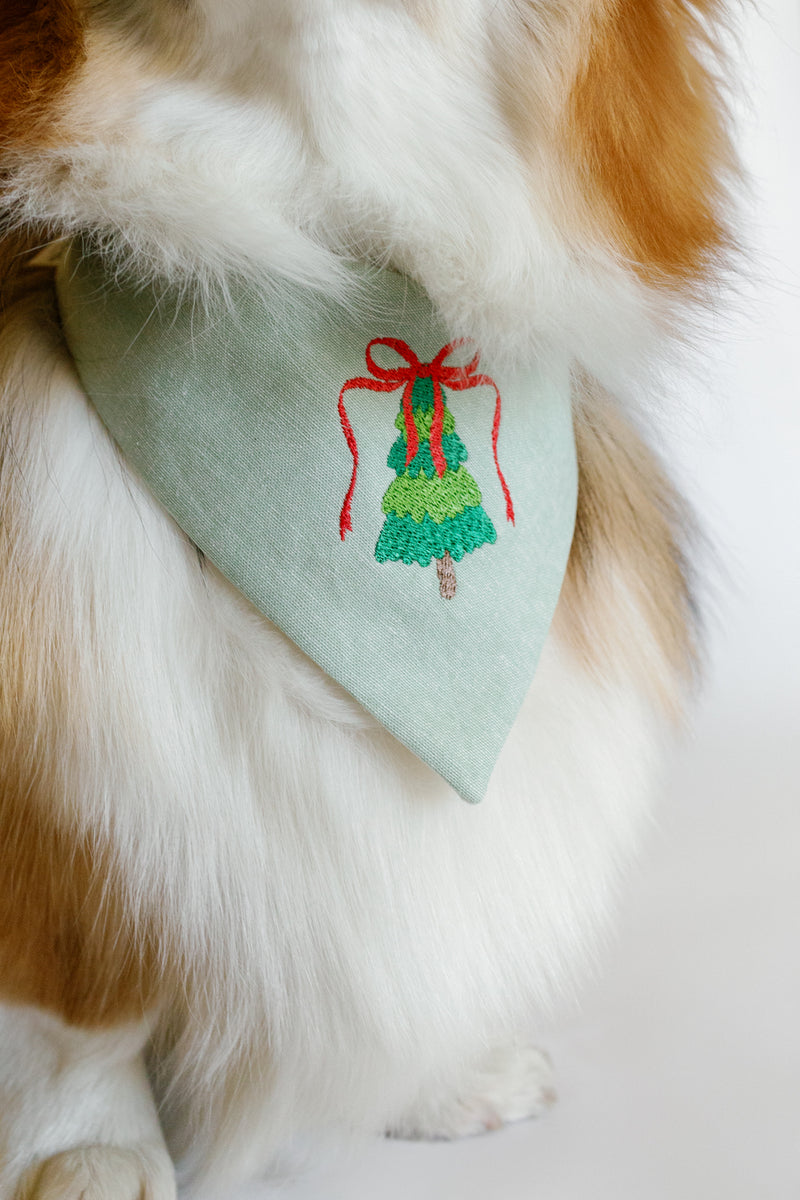 Dog wearing a green bandana with a embroidered green tree design on a white background