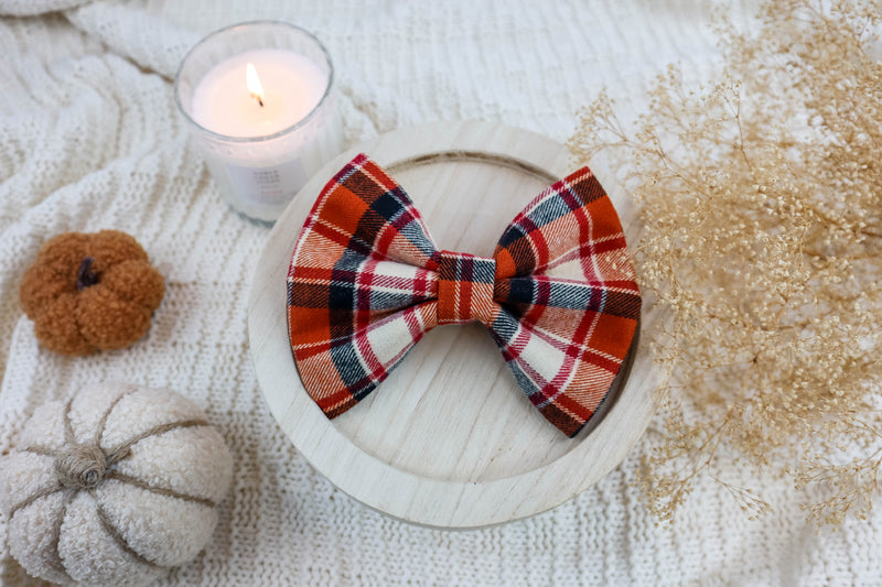 Plaid bow tie on a wooden plate with pumpkins and a candle in the background