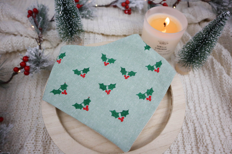 green dog bandana with holly pattern on a wooden plate, surrounded by Christmas decorations.