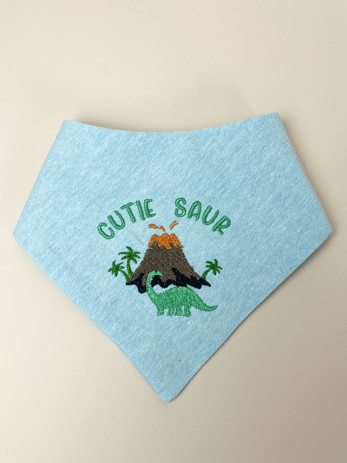 Light blue bandana with dinosaur design and 'Cutie Saur' text on a beige background