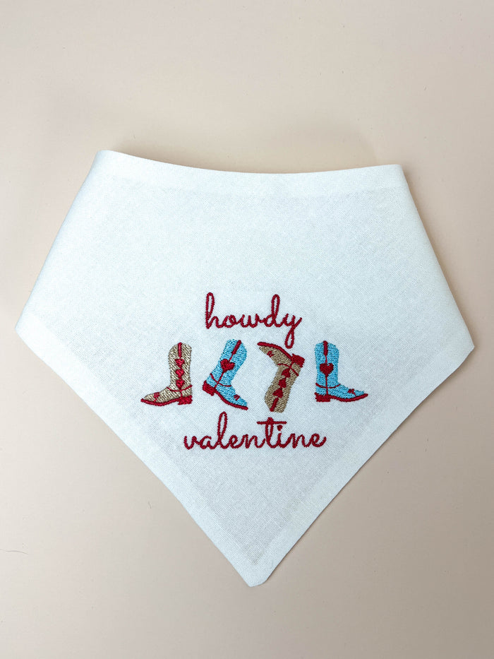 White bib with embroidered text and boot designs on a beige background
