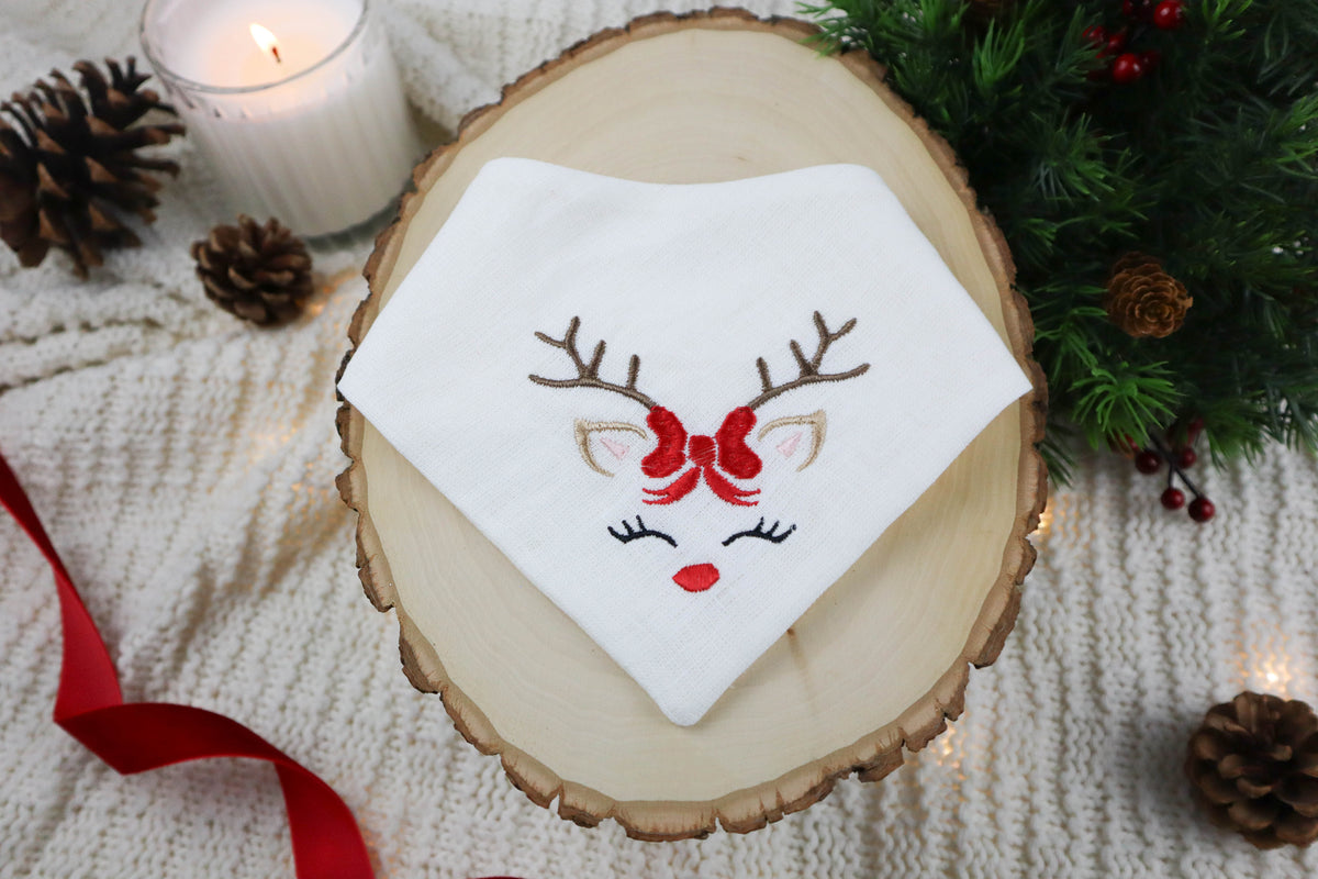 Embroidered bandana with reindeer design on a wooden surface with Christmas decorations.