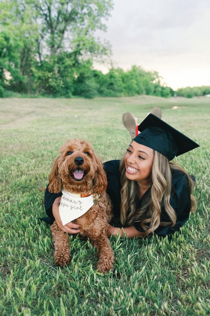 Graduate in cap and gown with a dog on a grassy field