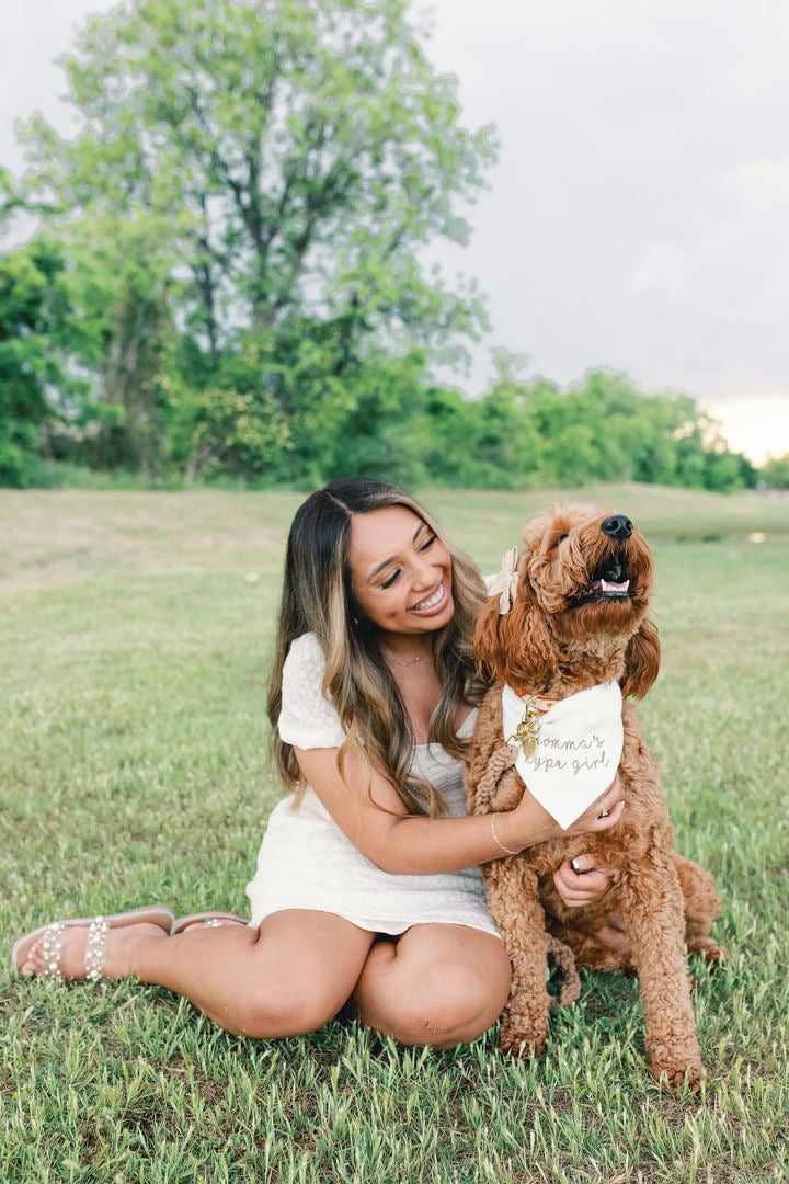 Woman sitting on grass with a dog wearing a bandana in a park