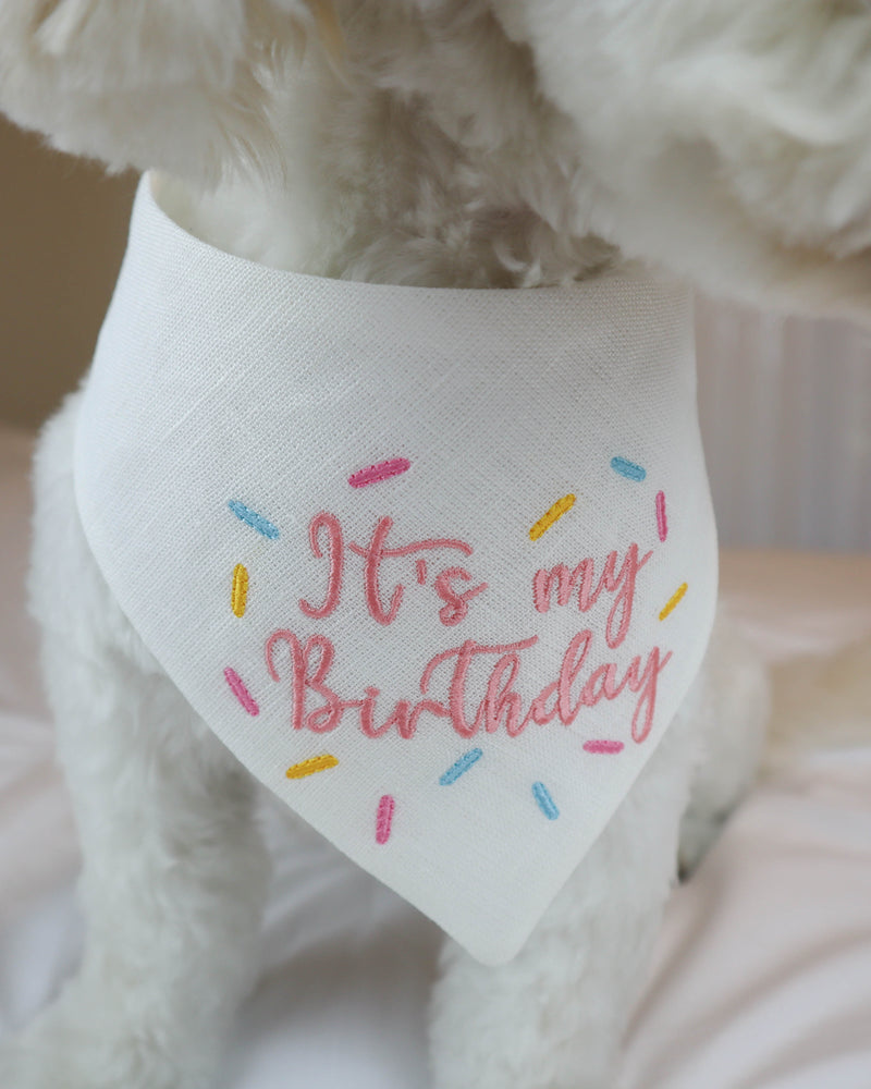 White dog wearing a bandana with 'It's my Birthday' text on a light background