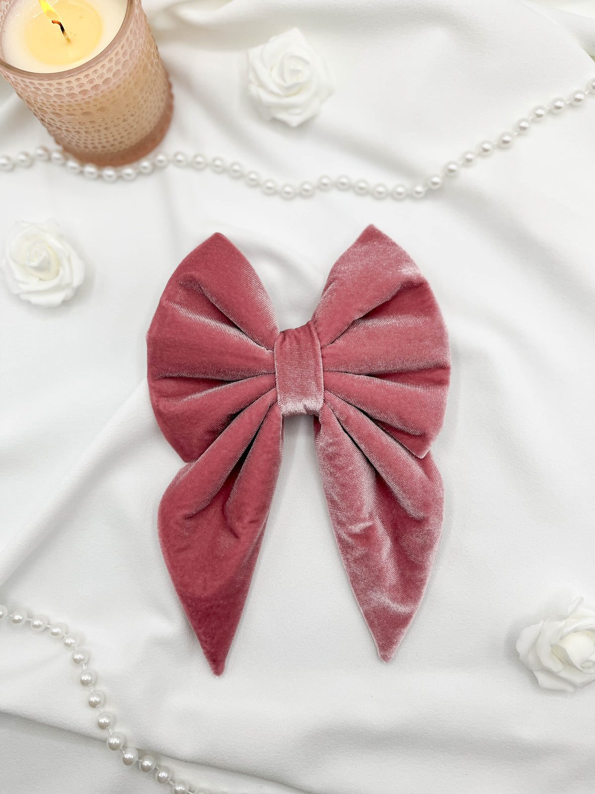 Pink velvet bow on a white surface with candles and pearls in the background