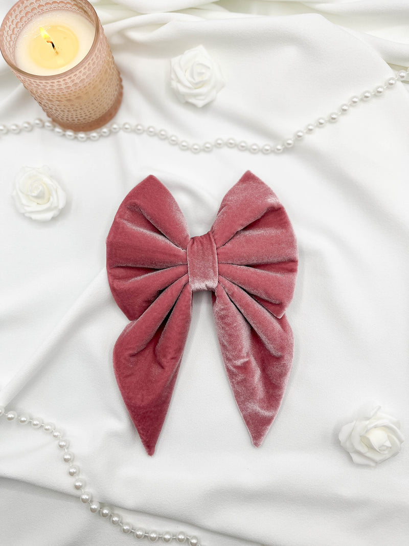 Pink velvet bow on a white fabric background with candles and flowers.