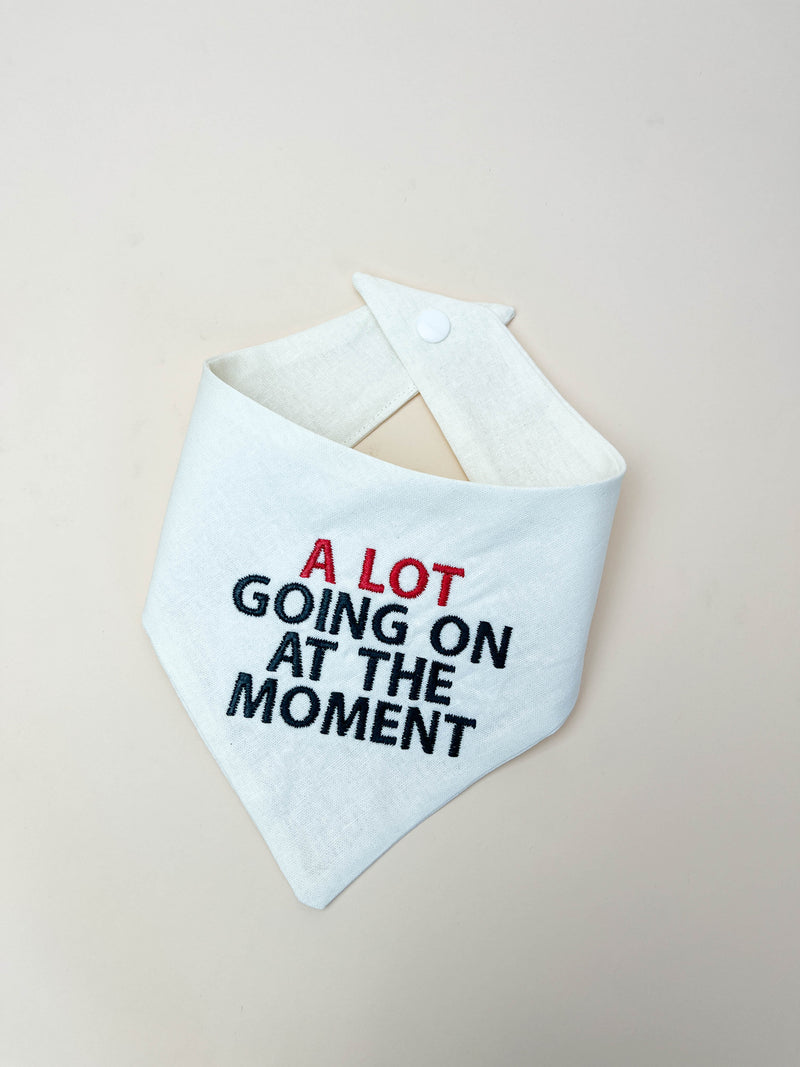 White bandana bib with text 'A Lot Going On At The Moment' on a beige background