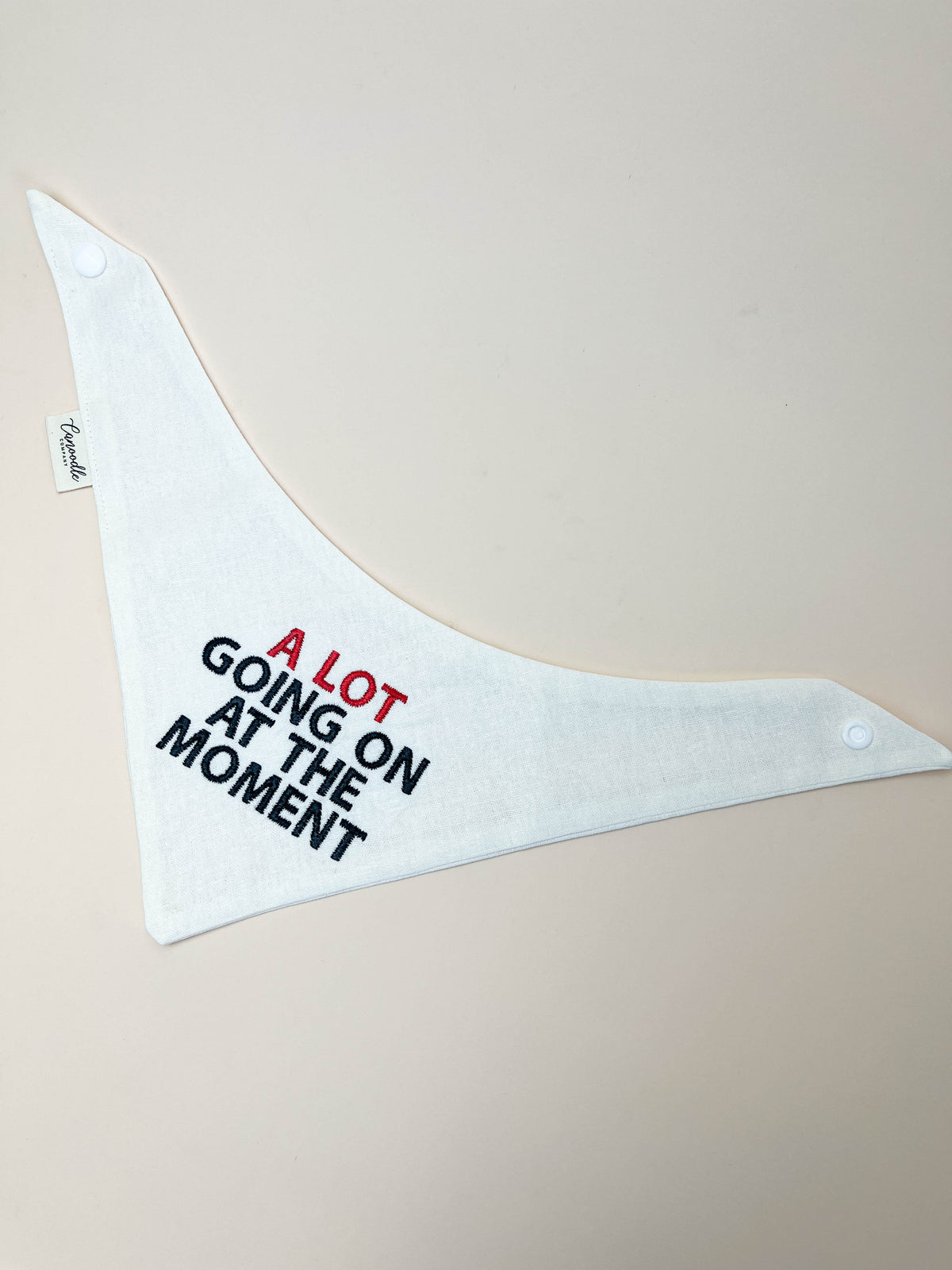 White bandana with text 'A LOT GOING ON AT THE MOMENT' on a beige background