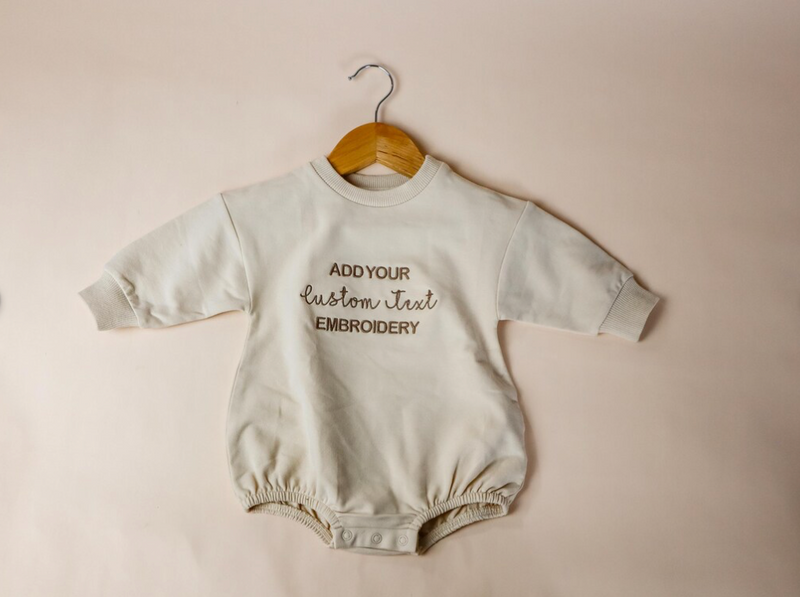 custom embroidered Baby romper with text on a hanger against a beige background